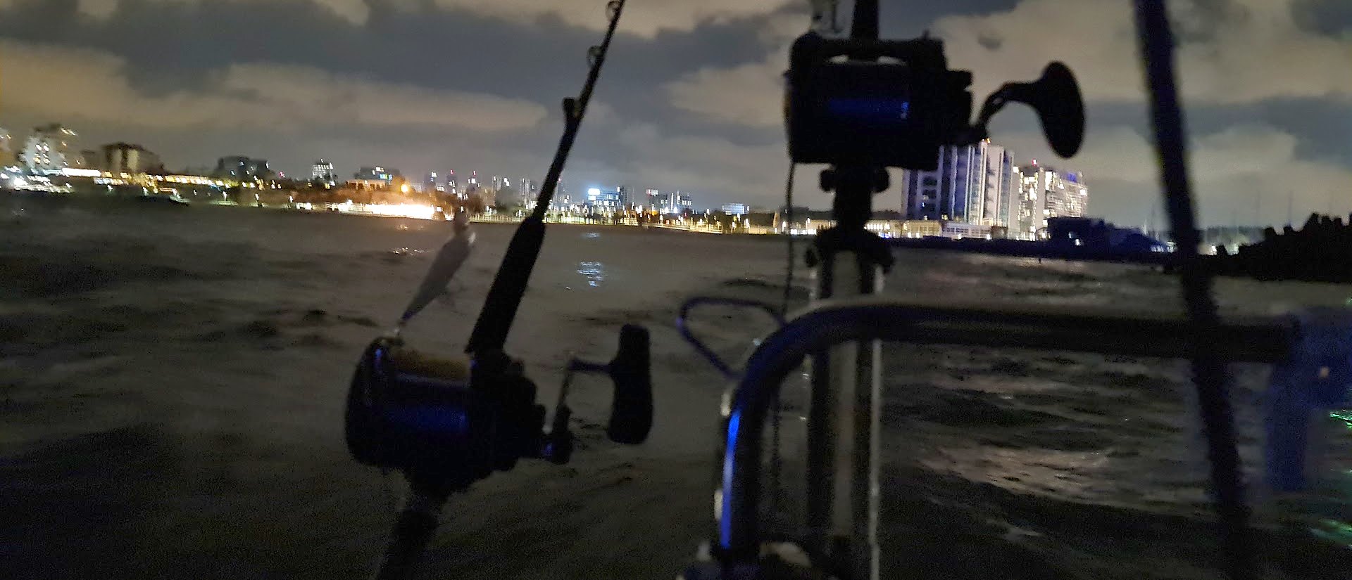 Fishing rods and reels on a boat at night, city lights on the shore